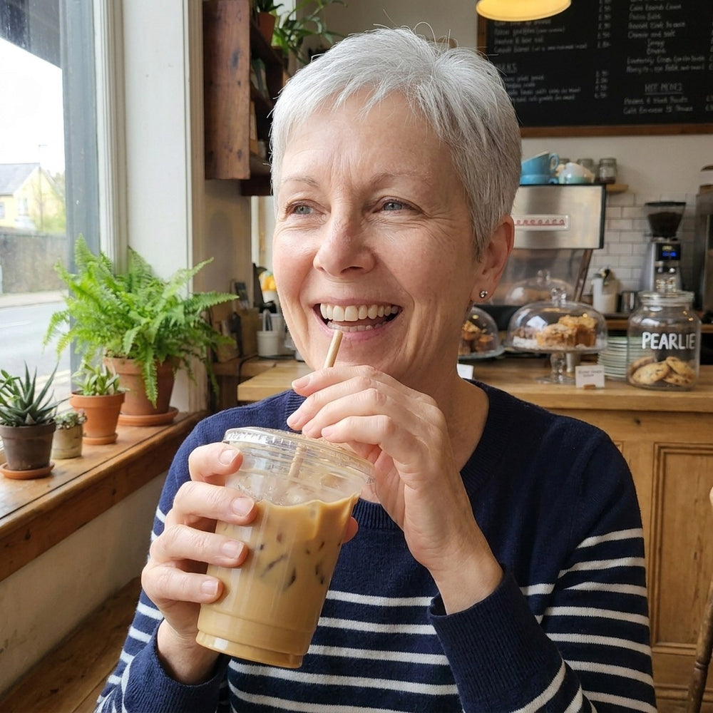A woman of 63 laughing with a bright smile over an iced coffee in a café