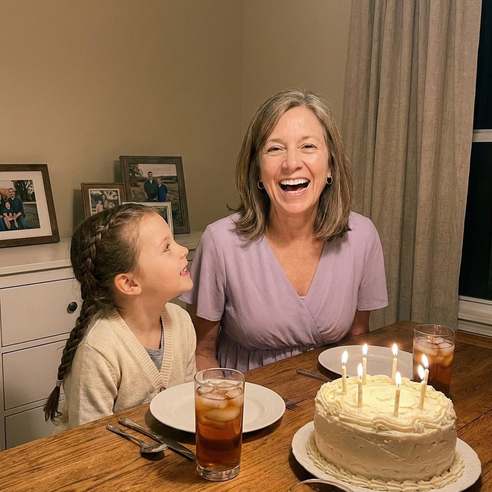 A grandmother laughing with a white smile at her birthday dinner while her granddaughter looks up at her